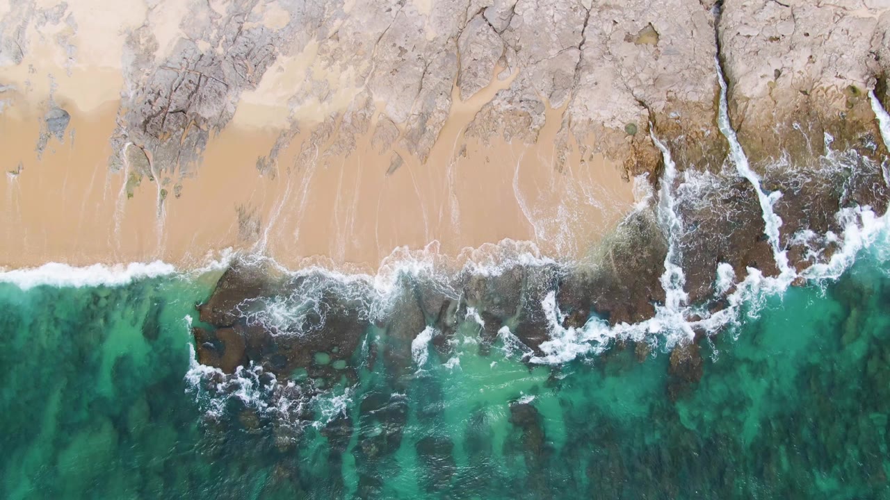 Overhead turquoise waves breaking against rocks and sand.