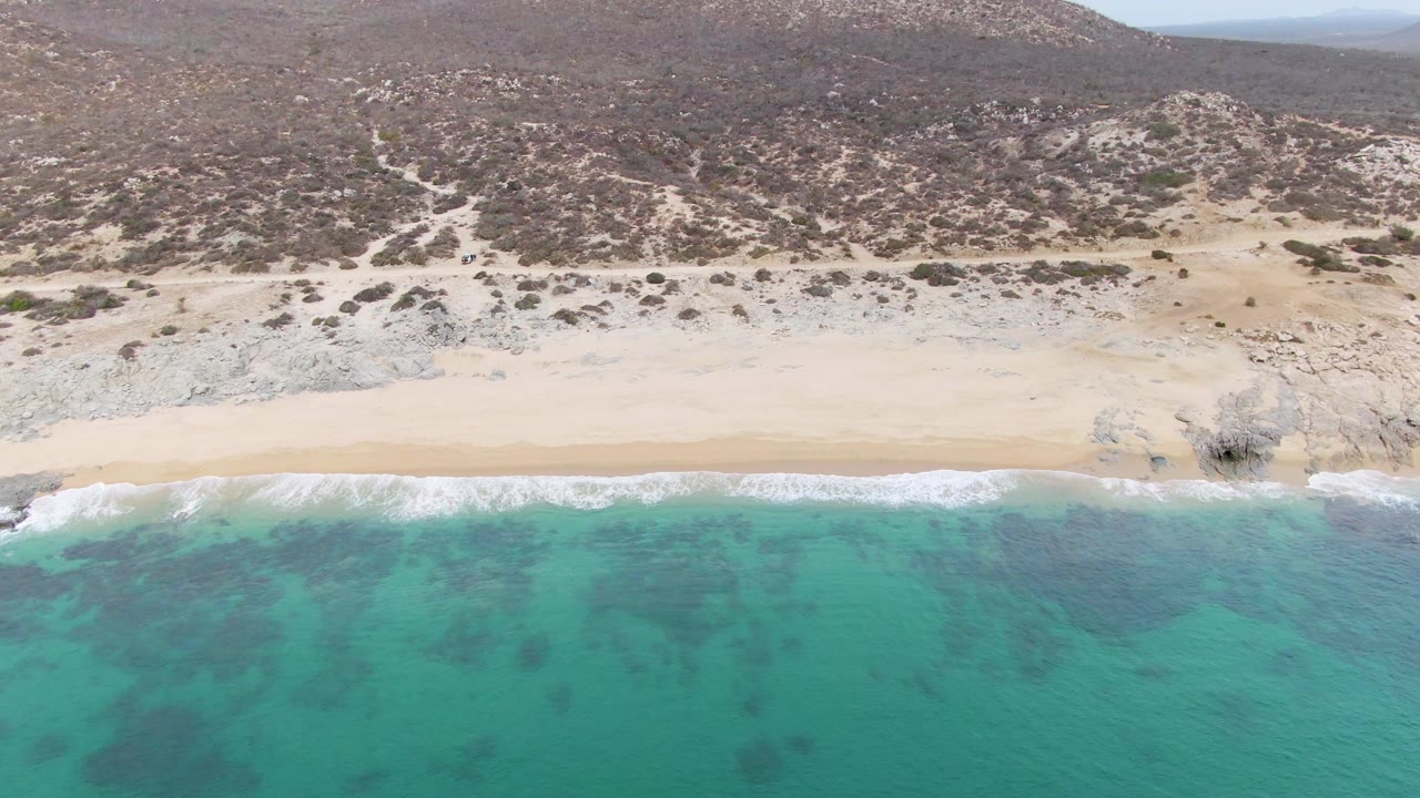 Aerial coastline with surf line, sand, rocks, and dry brush