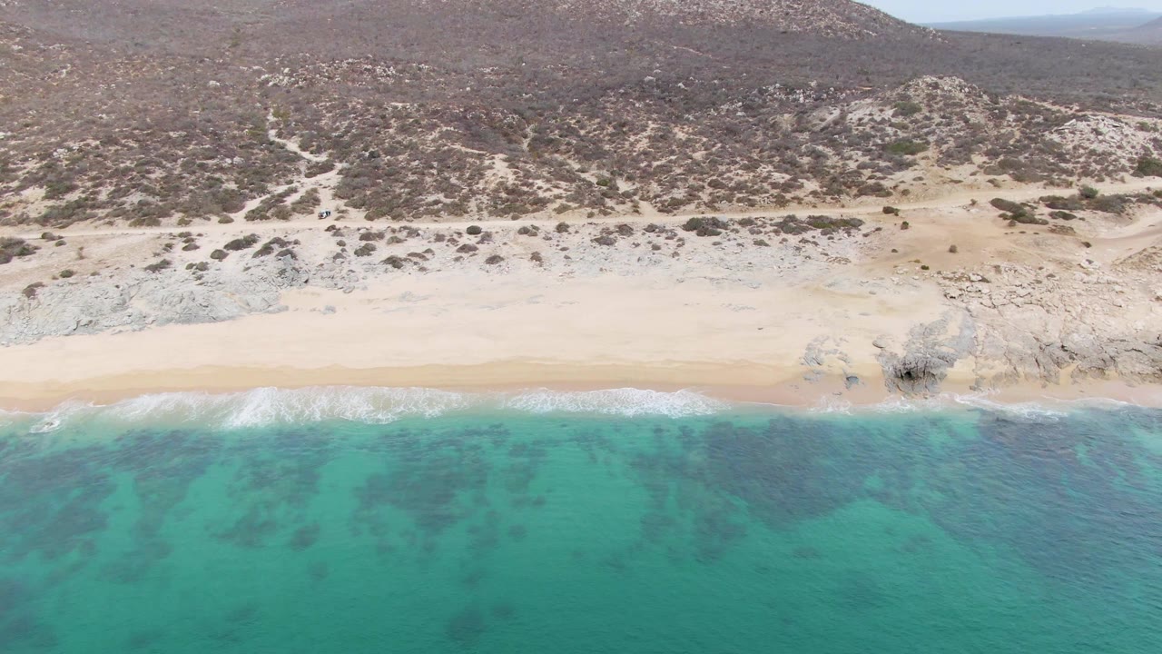 Aerial view of turquoise water reaching a sandy beach below rocky hills