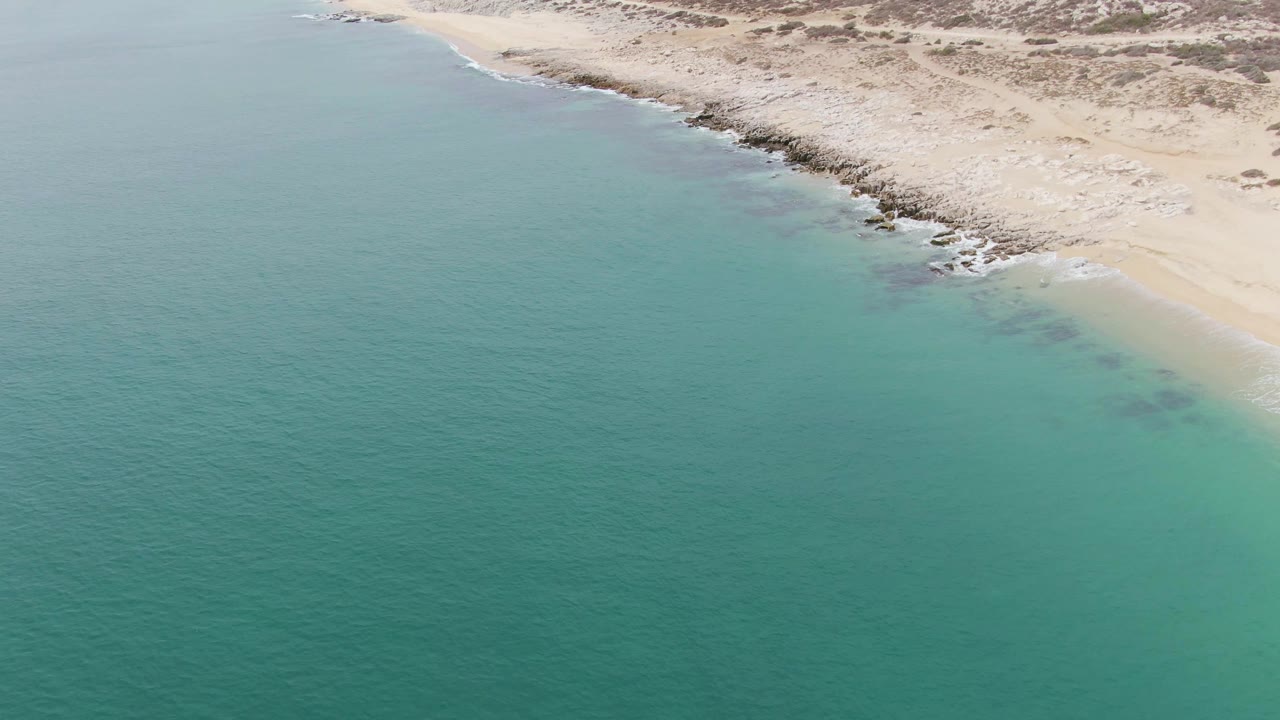 Turquoise water borders pale beach with dark rocks along the coast.