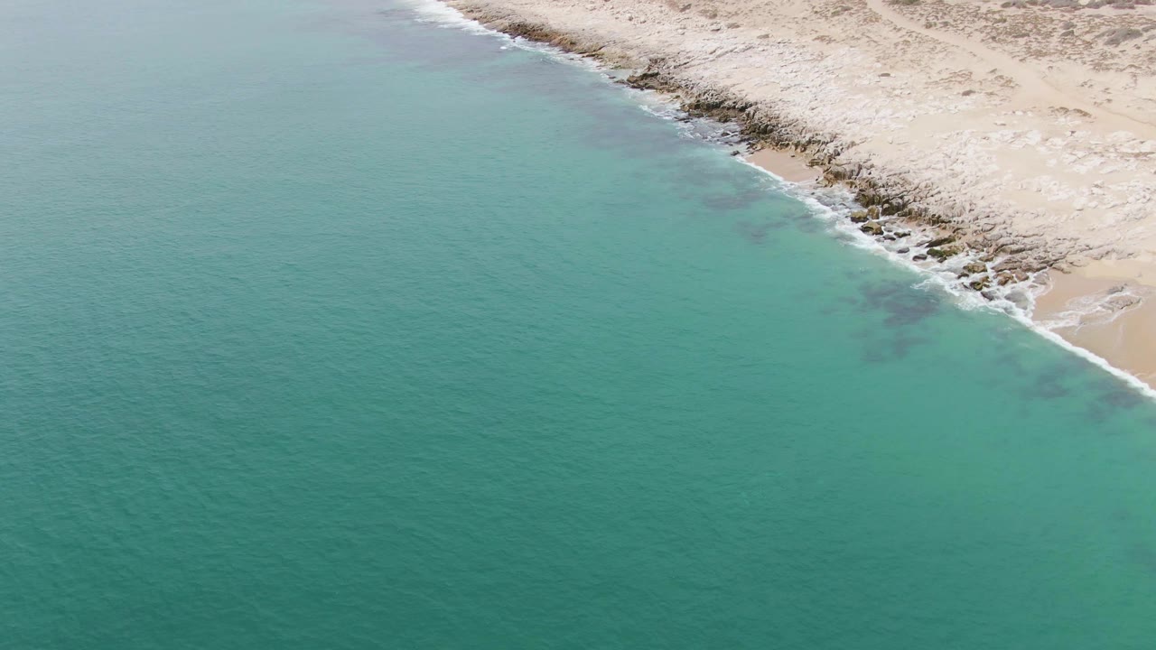 Aerial view of turquoise water beside a pale rocky shoreline
