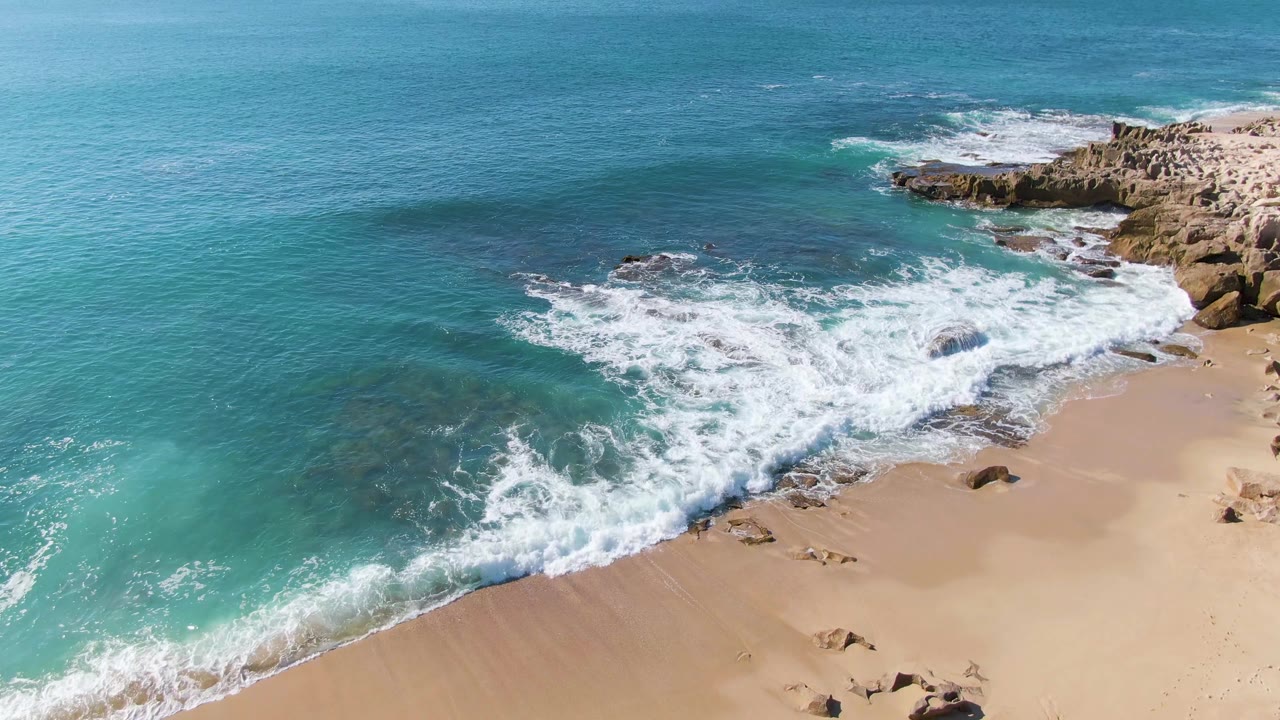 White wave foam spreading across a rocky shoreline and beach