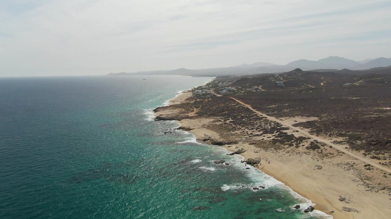 Drone view of surf rolling onto a rocky sandy beach
