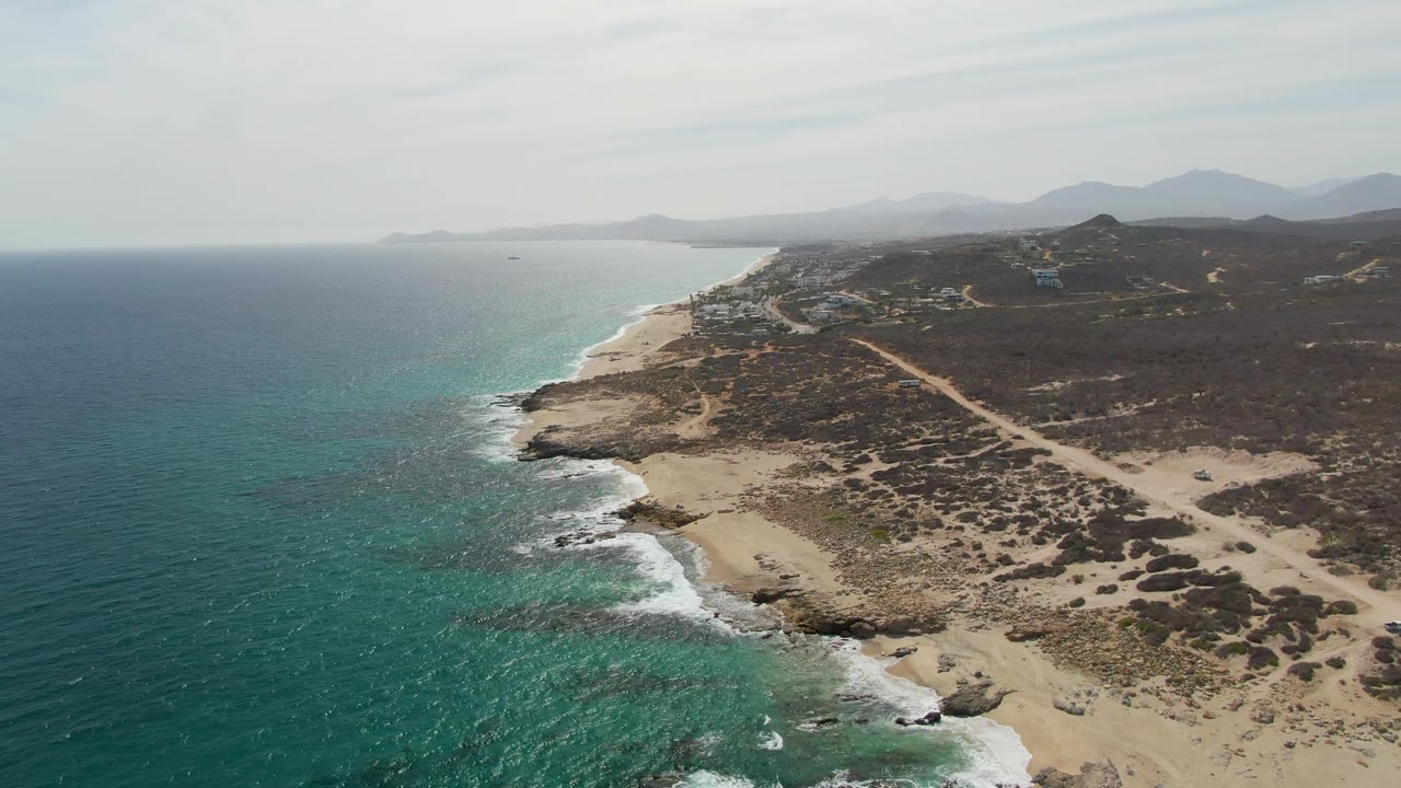 High aerial view of ocean surf along a rocky beach and scrub-covered coast.