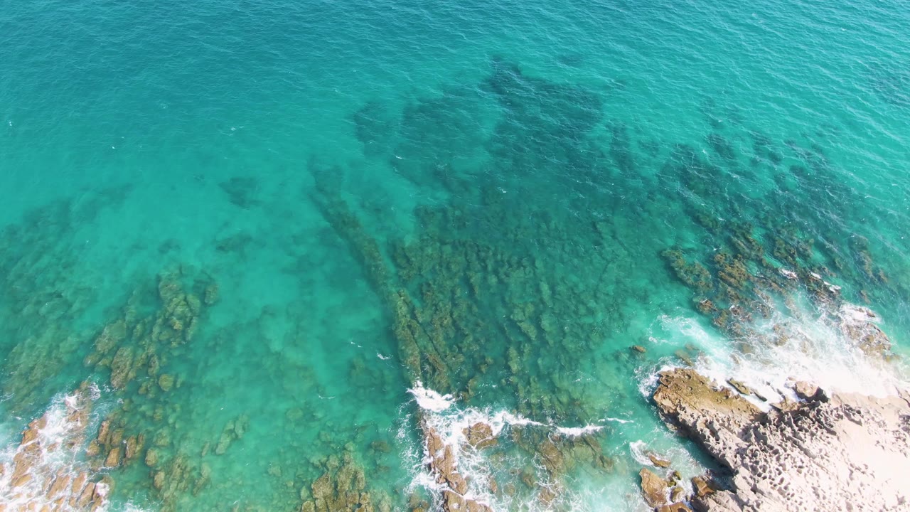 Turquoise water over rocks with wave foam near shore