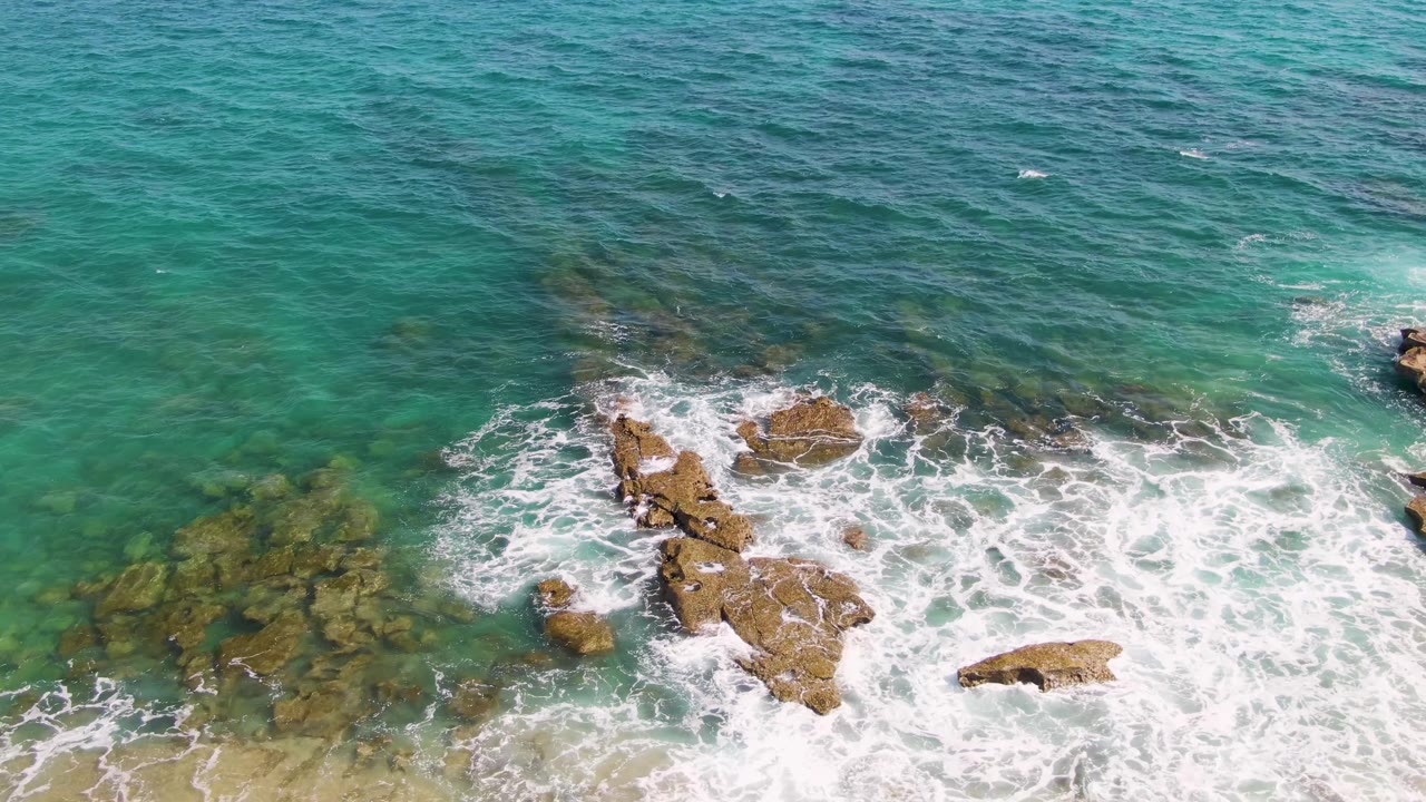 Turquoise surf spreads around a long rocky outcrop