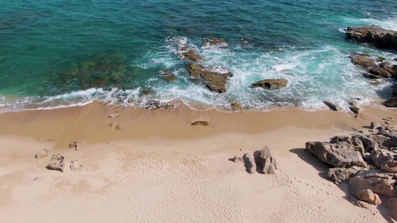 At 0:01, Punta Gorda Beach surf spreads farther across the rocks while the sandy lower frame remains empty with no visible people.
