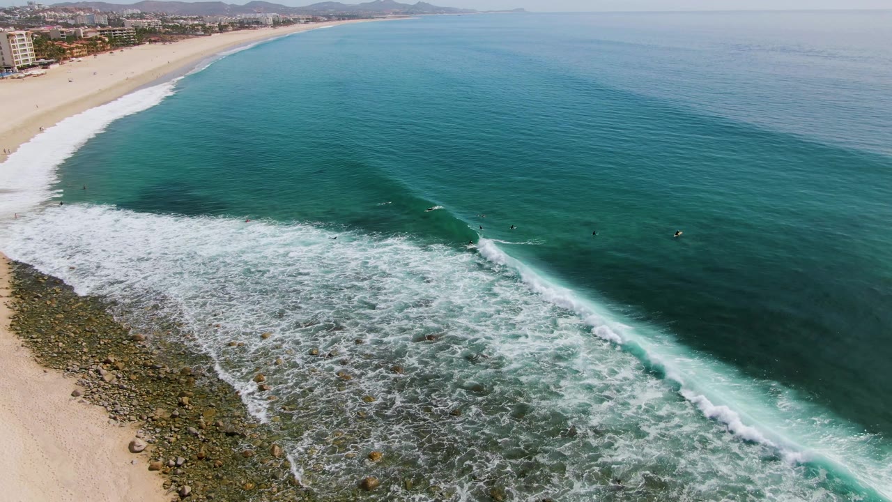 At 0:01, Punta Gorda Beach is seen from above as a diagonal band of white foam advances across blue-green water beside the rocky shore and sand.