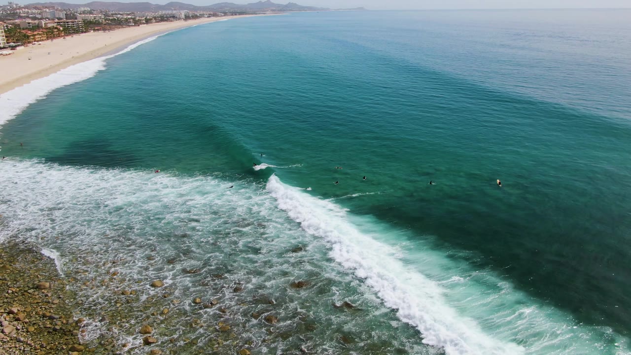 Aerial coastal frame with foam over rocks and open ocean beyond.