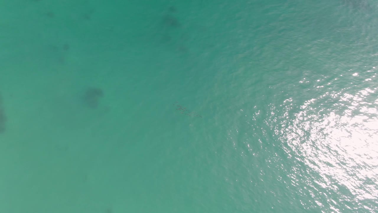 Top-down view of turquoise water at Punta Gorda Beach with bright reflection on the right, faint underwater patches, and no visible people.