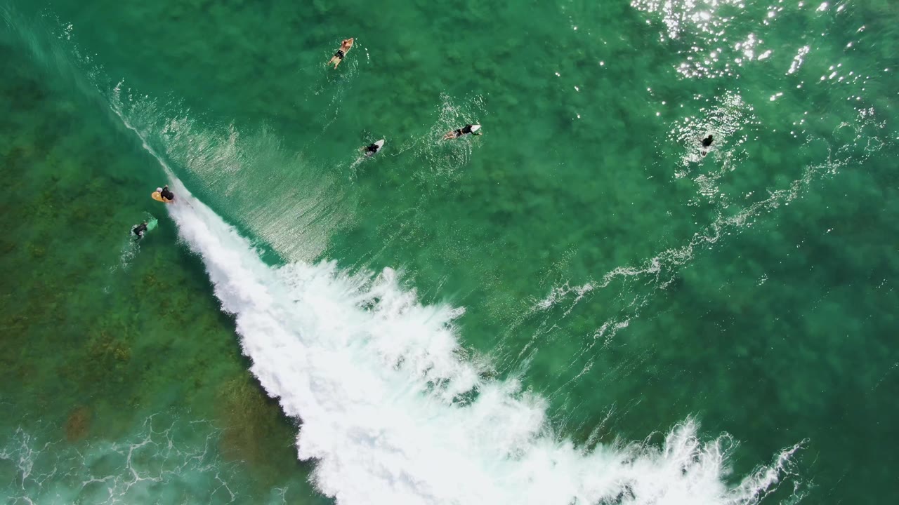 Breaking wave foam crosses the lower frame with surfers above it.