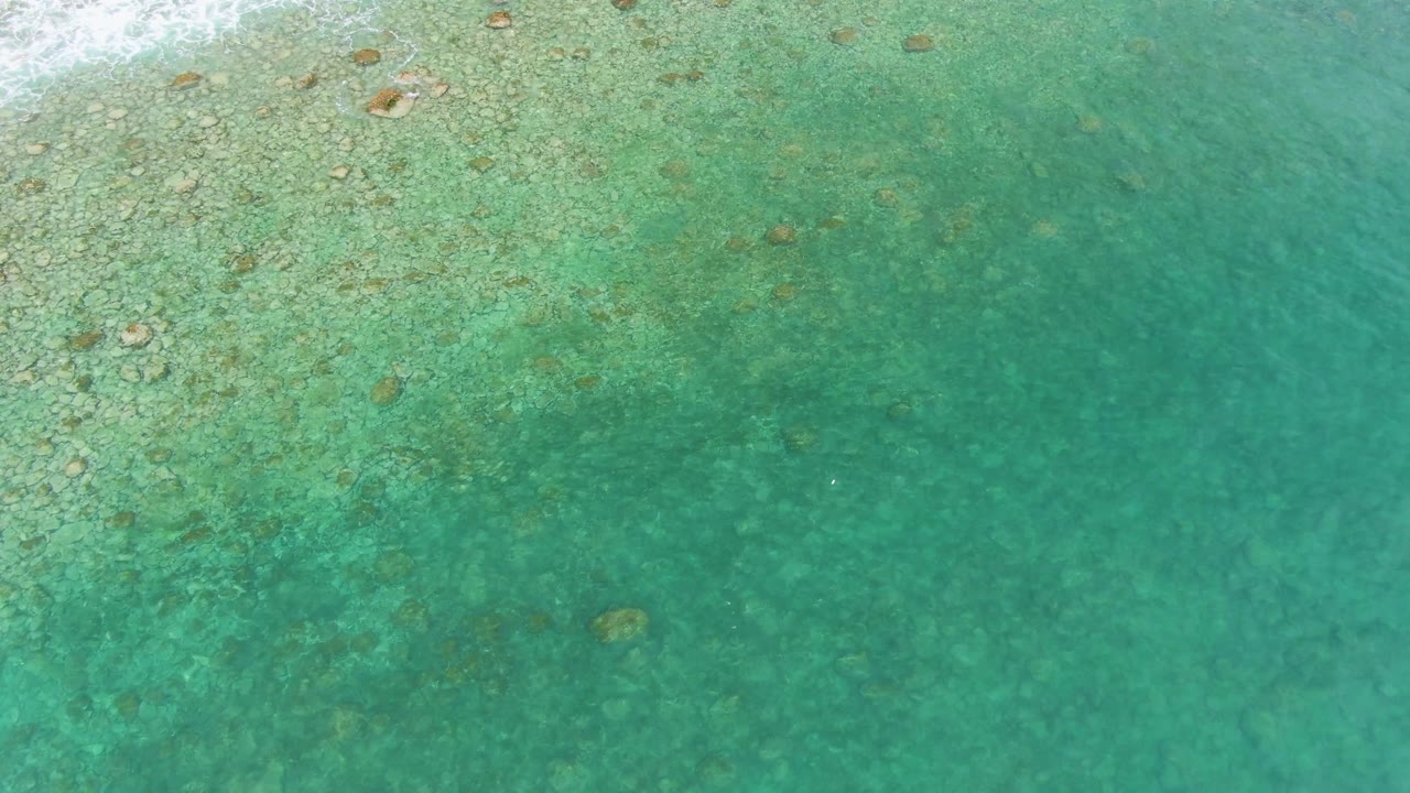 Clear green-blue water with pale reef patches and scattered rocks.