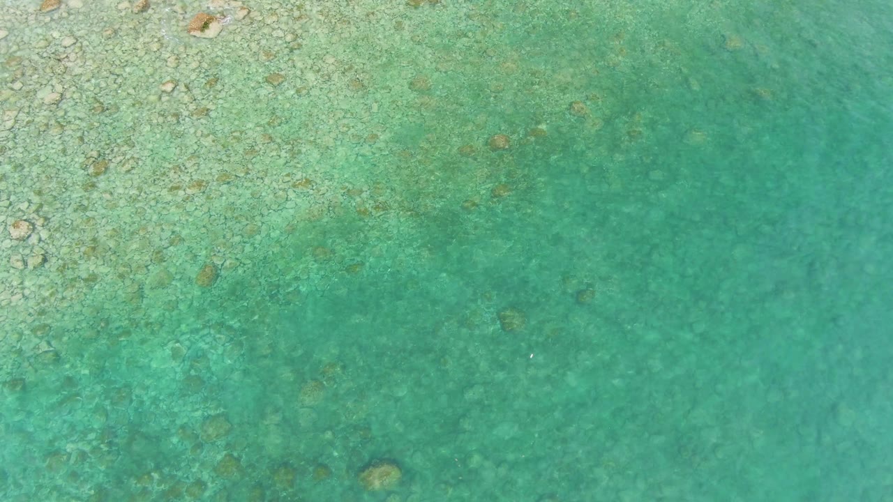 Overhead view at Punta Gorda Beach with textured reef and small rocks concentrated along the left and upper areas while smoother turquoise water fills the right side, no visible people.