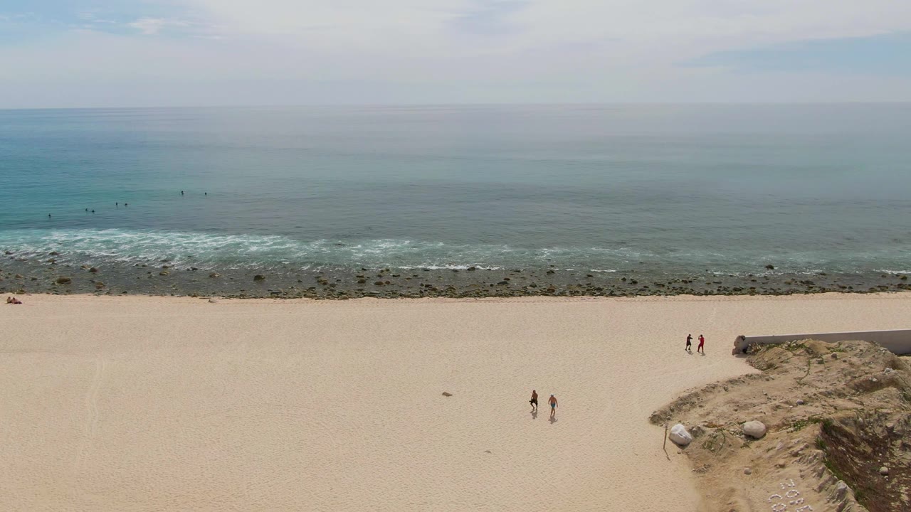 Open beach and ocean with several small walkers near rocky shore.