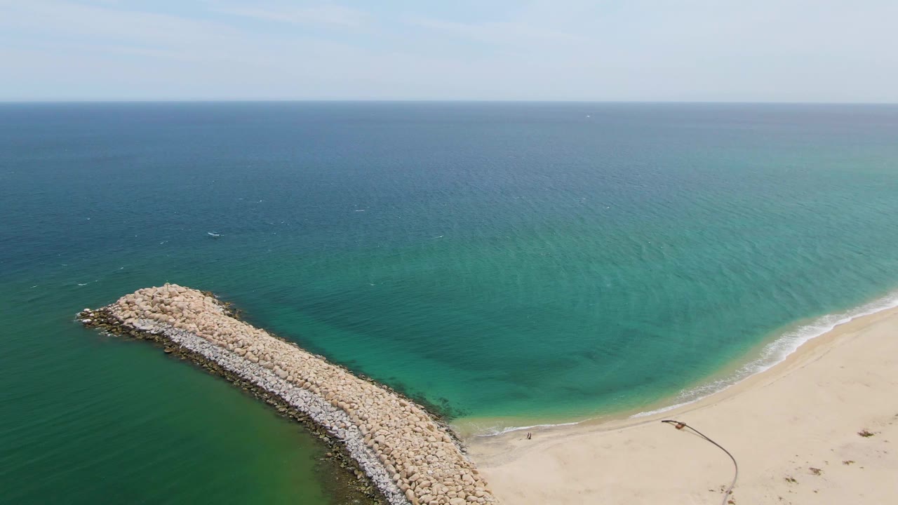 Breakwater rocks beside sandy shoreline and turquoise shallows