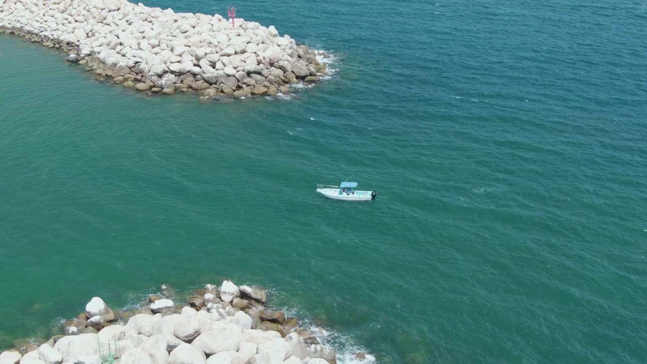 Small boat on green-blue water between rocky breakwaters.