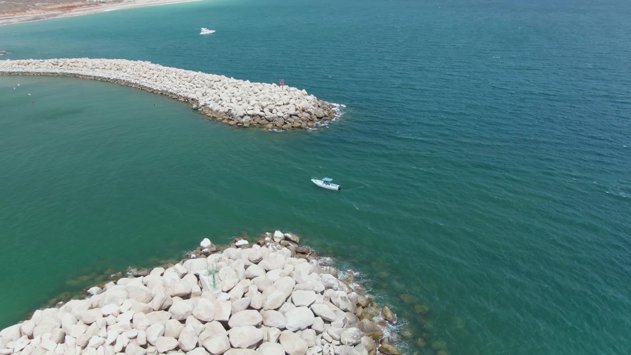 Rock breakwater and small boat seen from above in green ocean water.