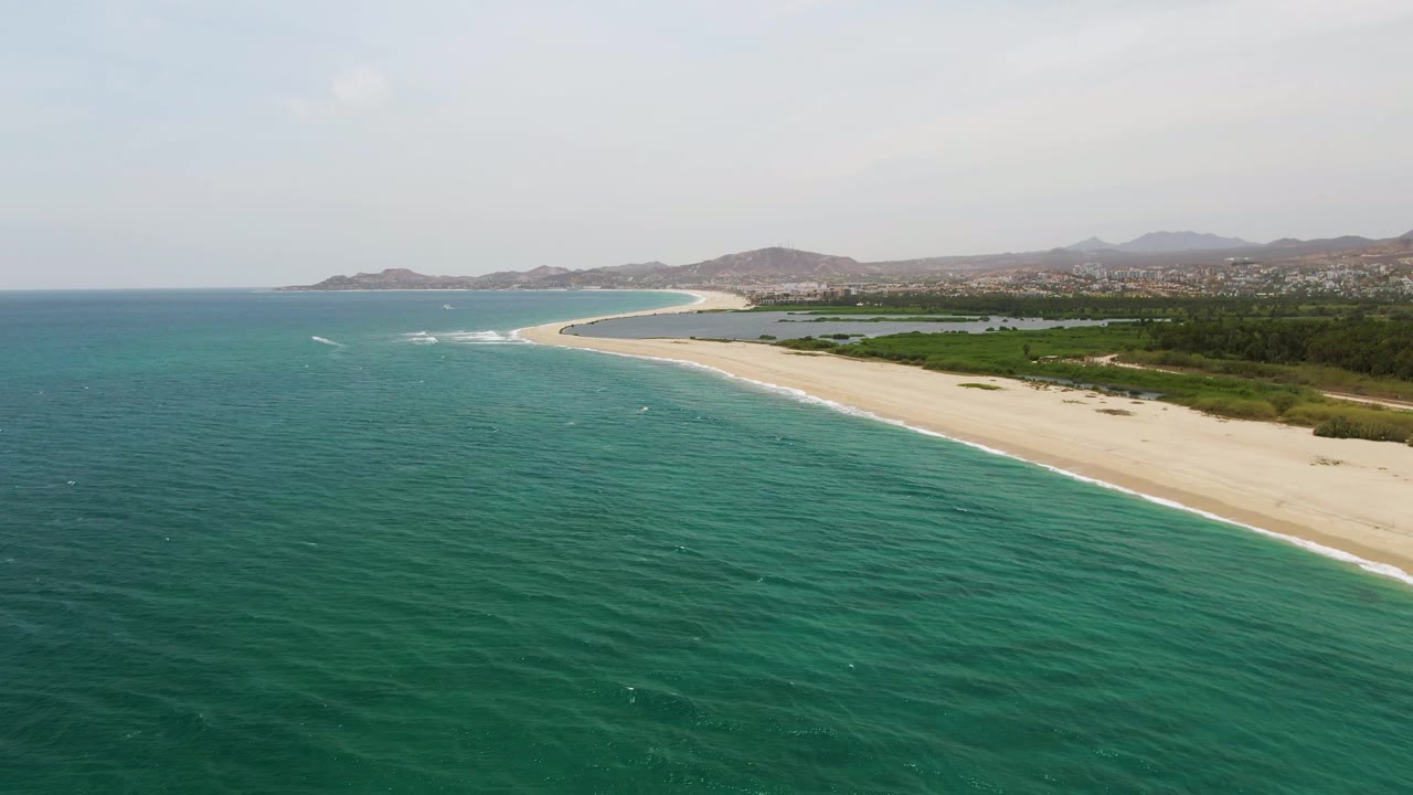 Aerial beach shoreline with open turquoise sea and green land behind the sand.