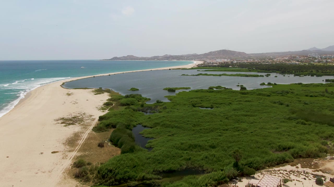 Aerial view of sandy beach, lagoon, green marsh, ocean waves, and distant hills.
