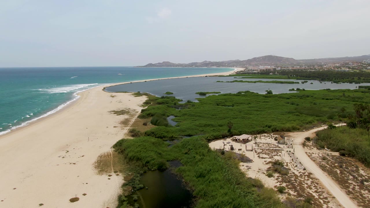 Aerial view of sandy beach, turquoise ocean, and green coastal wetlands.