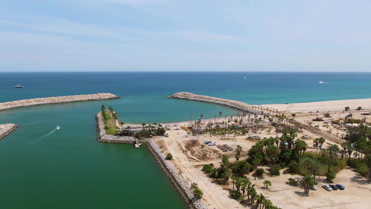 Aerial view of a small watercraft in a coastal channel beside rocky breakwaters and sandy beach.
