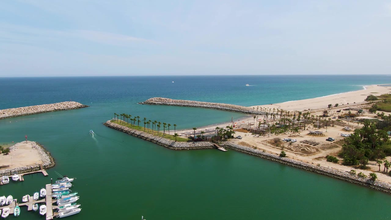 Third frame shows Puerto Los Cabos Beach from an elevated angle, with long rock breakwaters enclosing green water, a bright sandy shore to the right, boats at the lower edge, and no visible people.