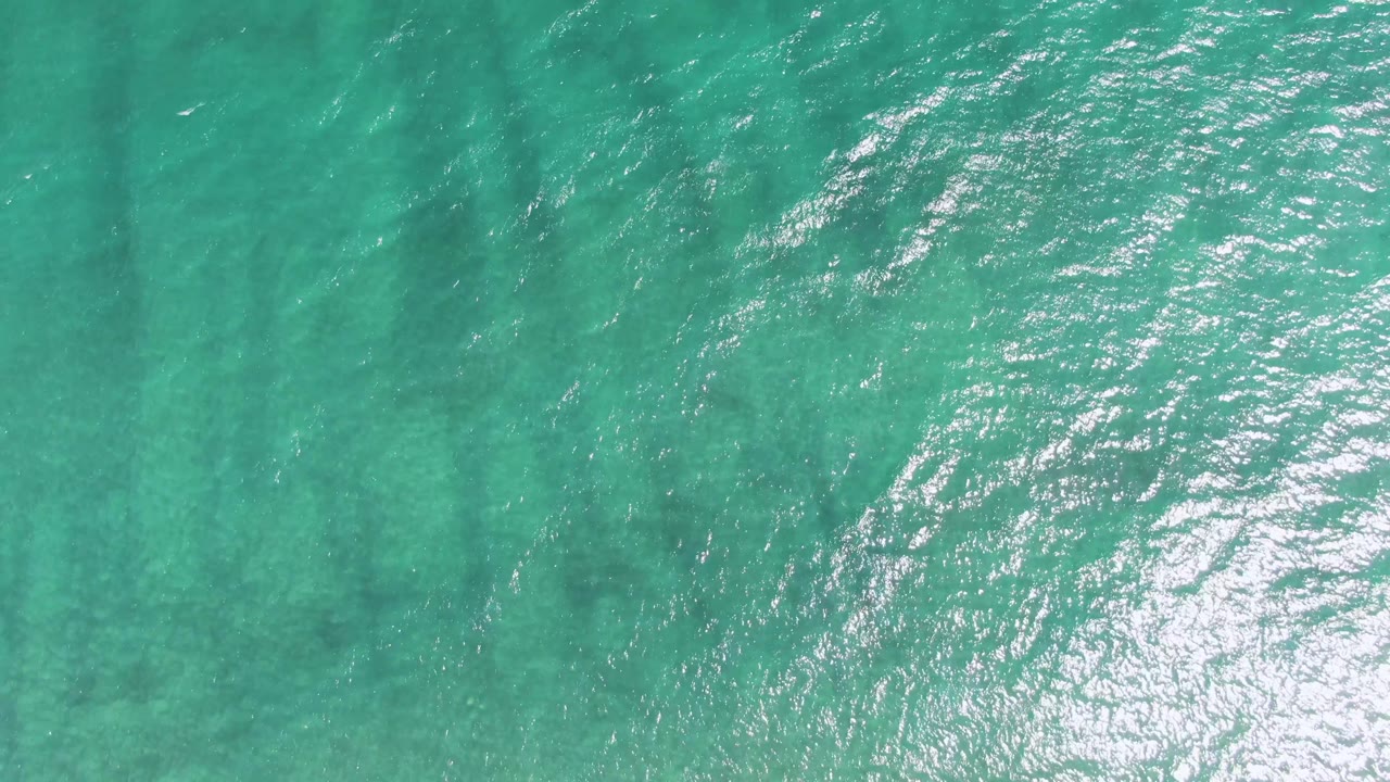 Turquoise ocean water with sun reflections and darker underwater streaks.