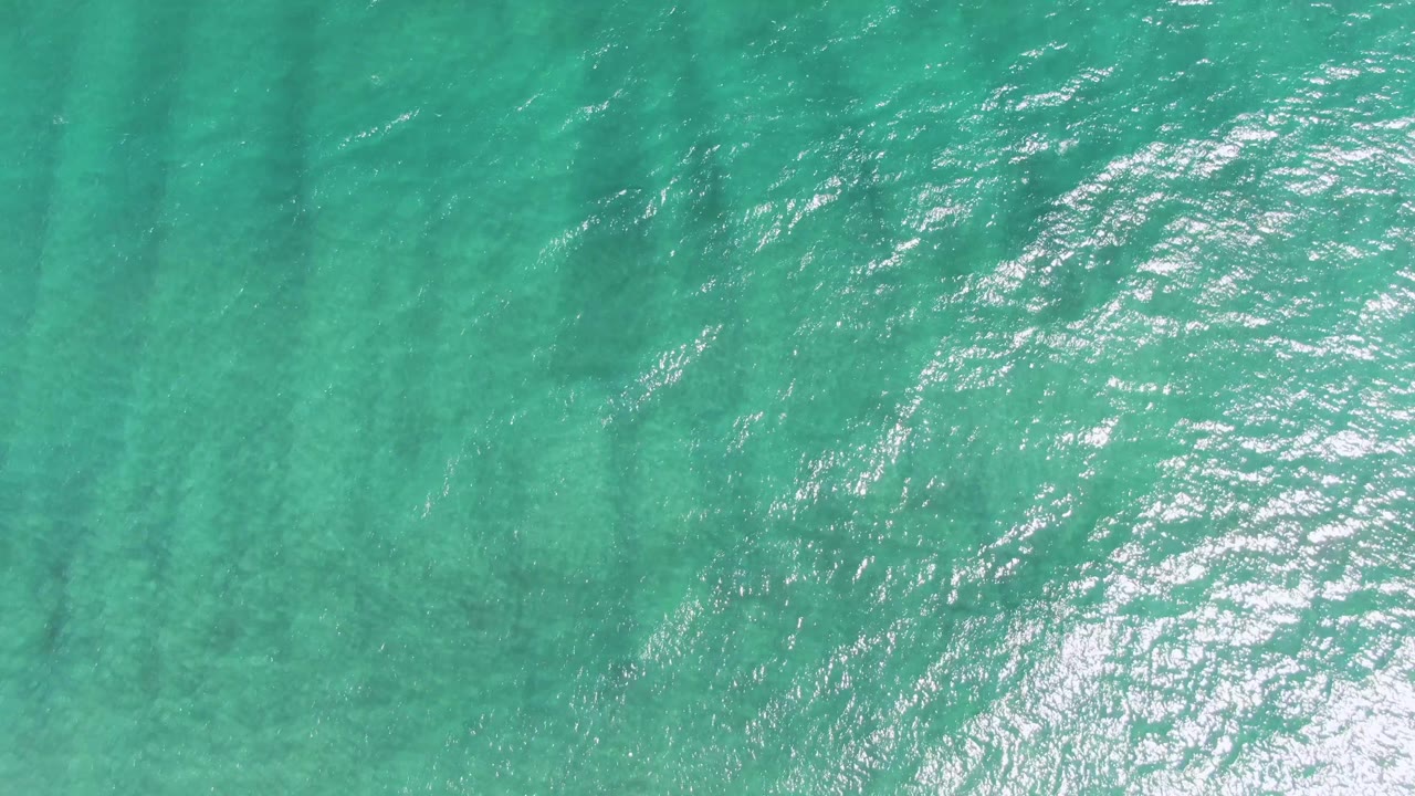 Clear green-blue water at Puerto Los Cabos Beach fills the frame, with small ripples, soft sun glints, and no visible people.