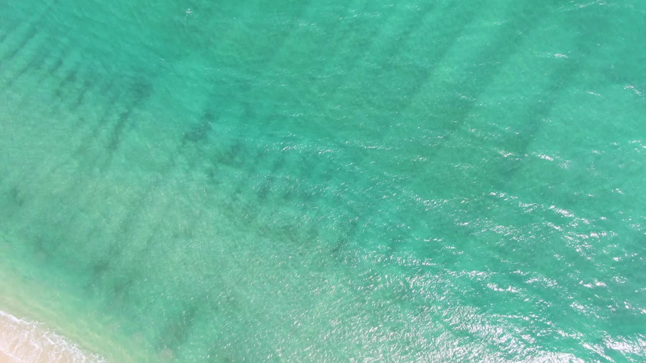Clear green-blue water with darker seabed streaks and a small wedge of sand at the bottom.
