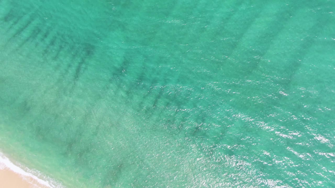 Puerto Los Cabos Beach shoreline seen from above as a narrow white foam line reaches the sand, with no visible people in frame.
