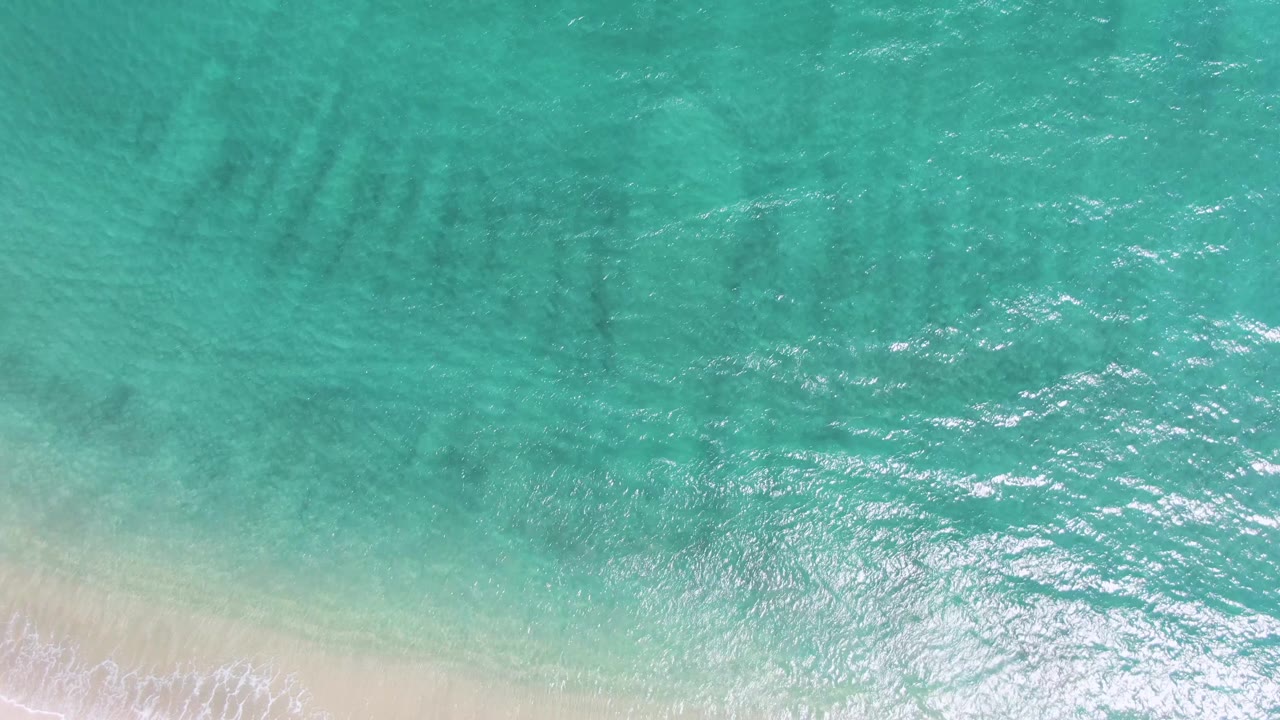 Turquoise ocean water over pale sand with a thin foam line at the beach edge.