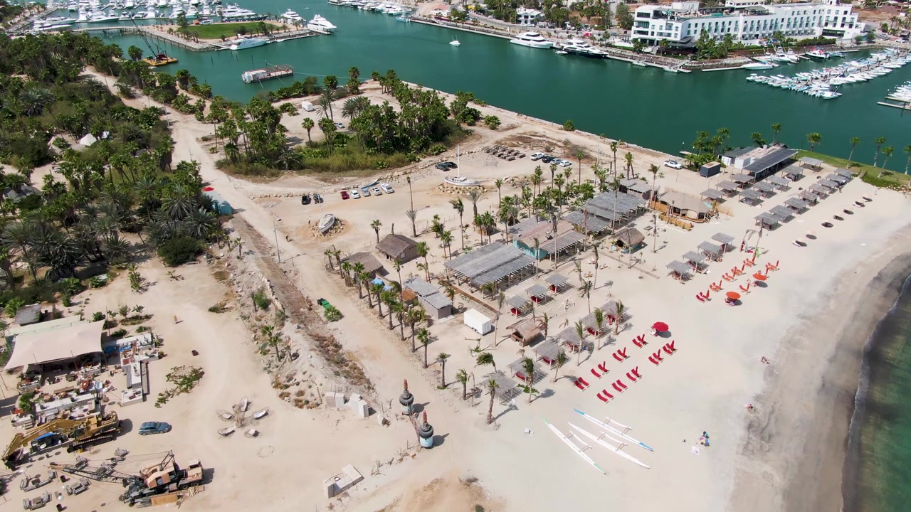 Aerial view of sandy beach construction beside marina water and boats.