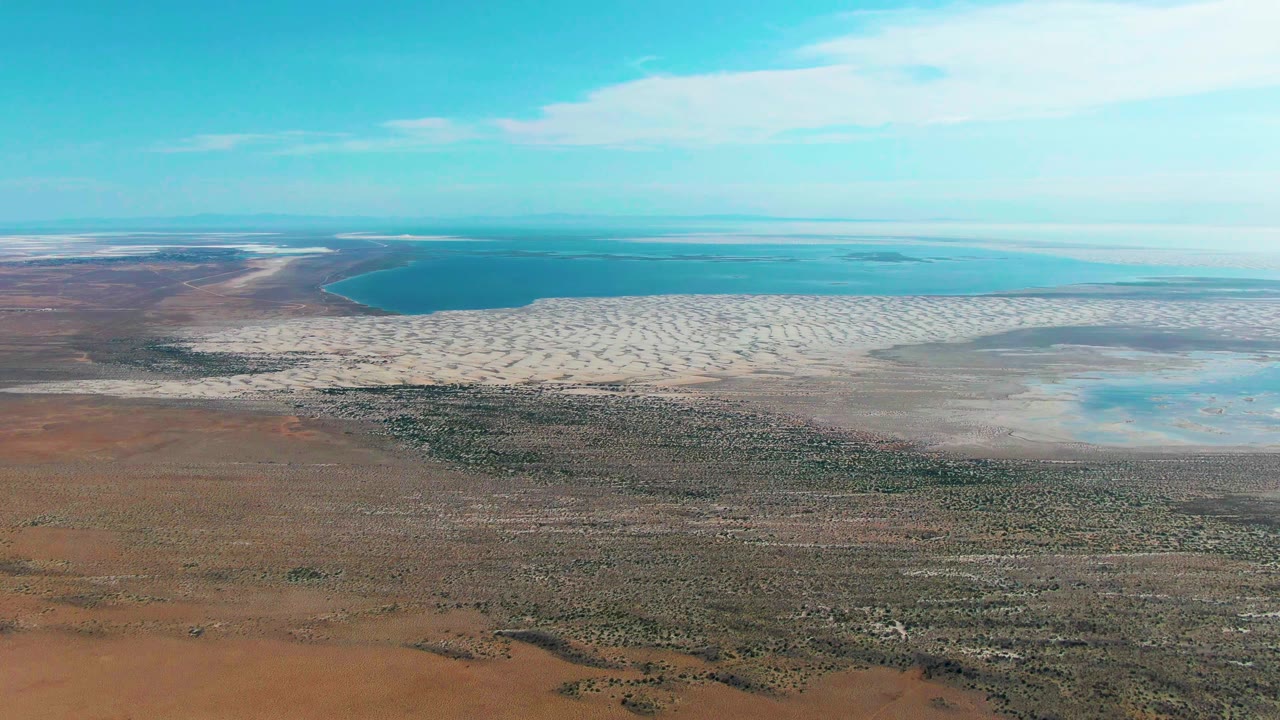 Aerial view of turquoise water, pale beach, and scrubby arid land.