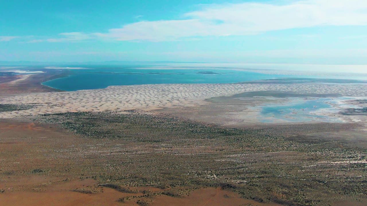 Arid plain and exposed pale shoreline below a wide blue sky.