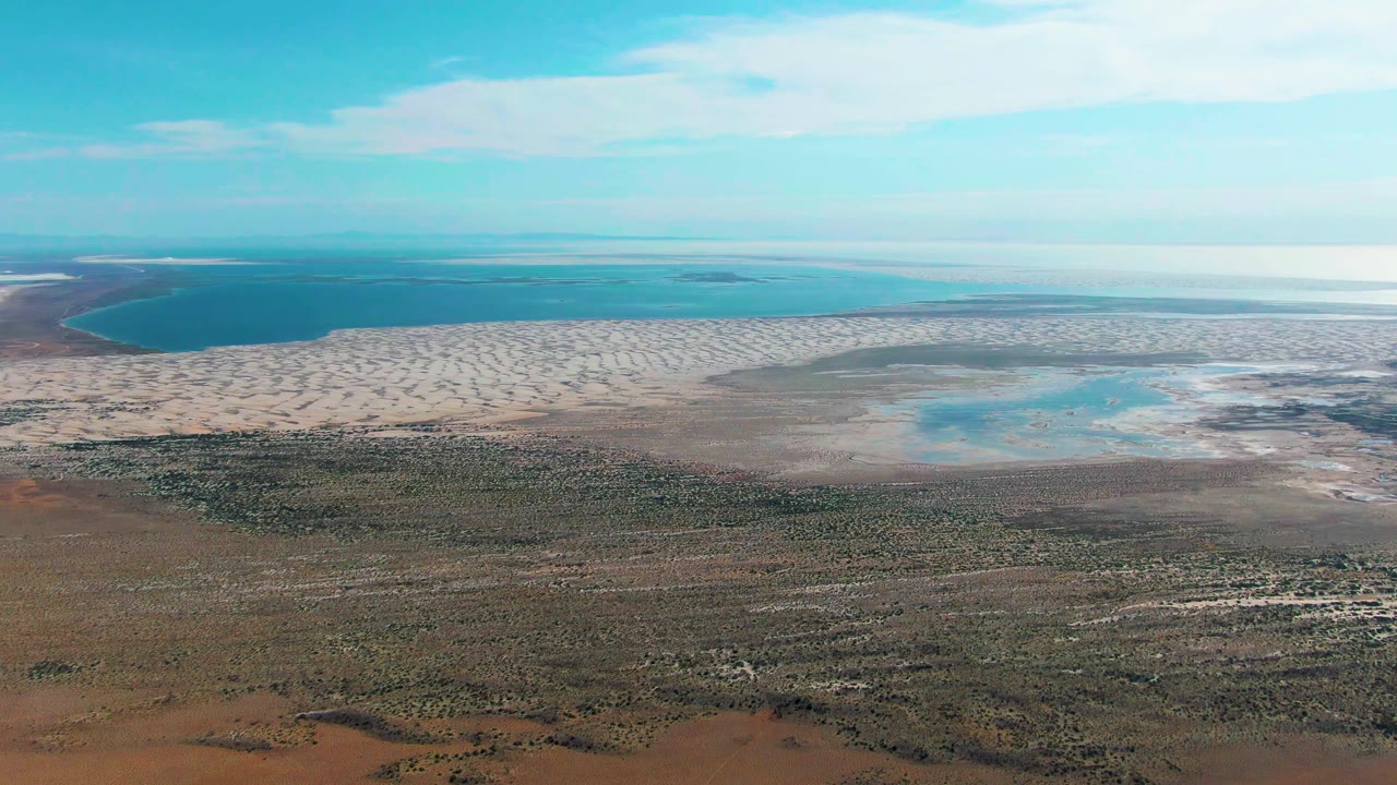 Aerial view of blue coastal water, pale tidal flats, and brown arid land.