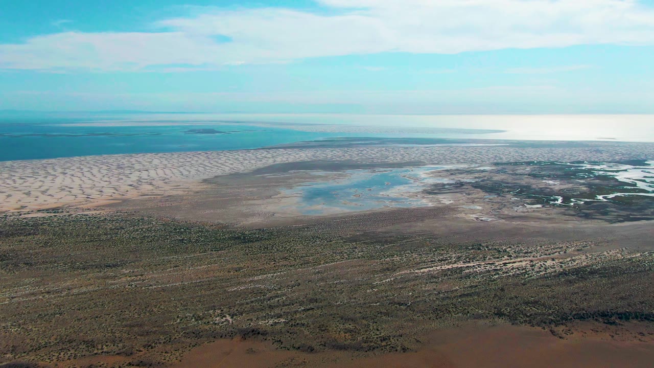 Aerial coastal landscape with dunes, shallow lagoon water, and scrub foreground.