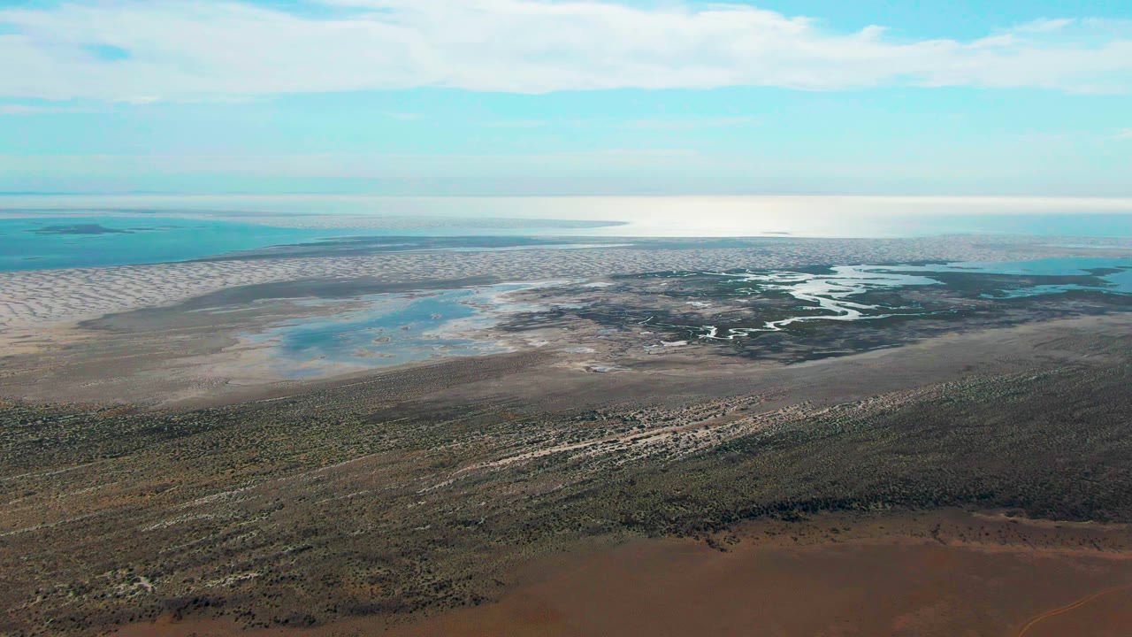 Aerial view over Guerrero Negro with winding water channels near the center, pale shoreline flats, open blue-green water, and no visible people.