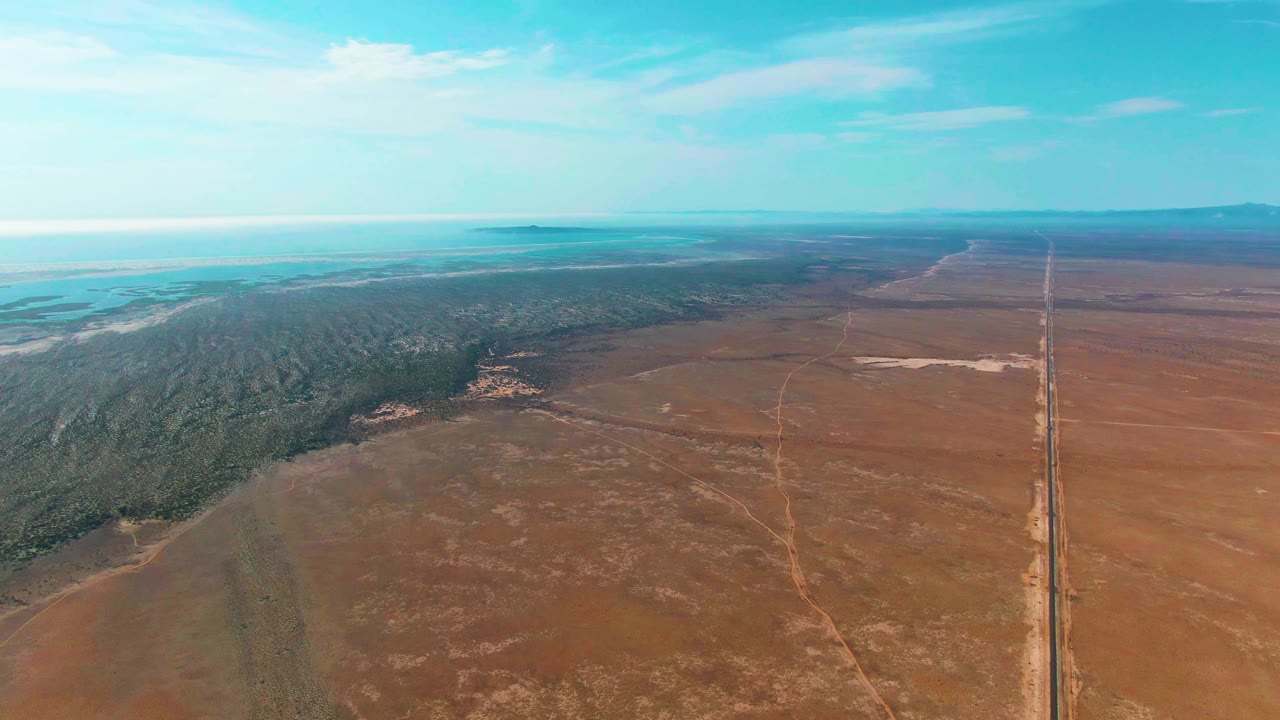 Drone perspective over dry rural land with forest on the left and a road on the right