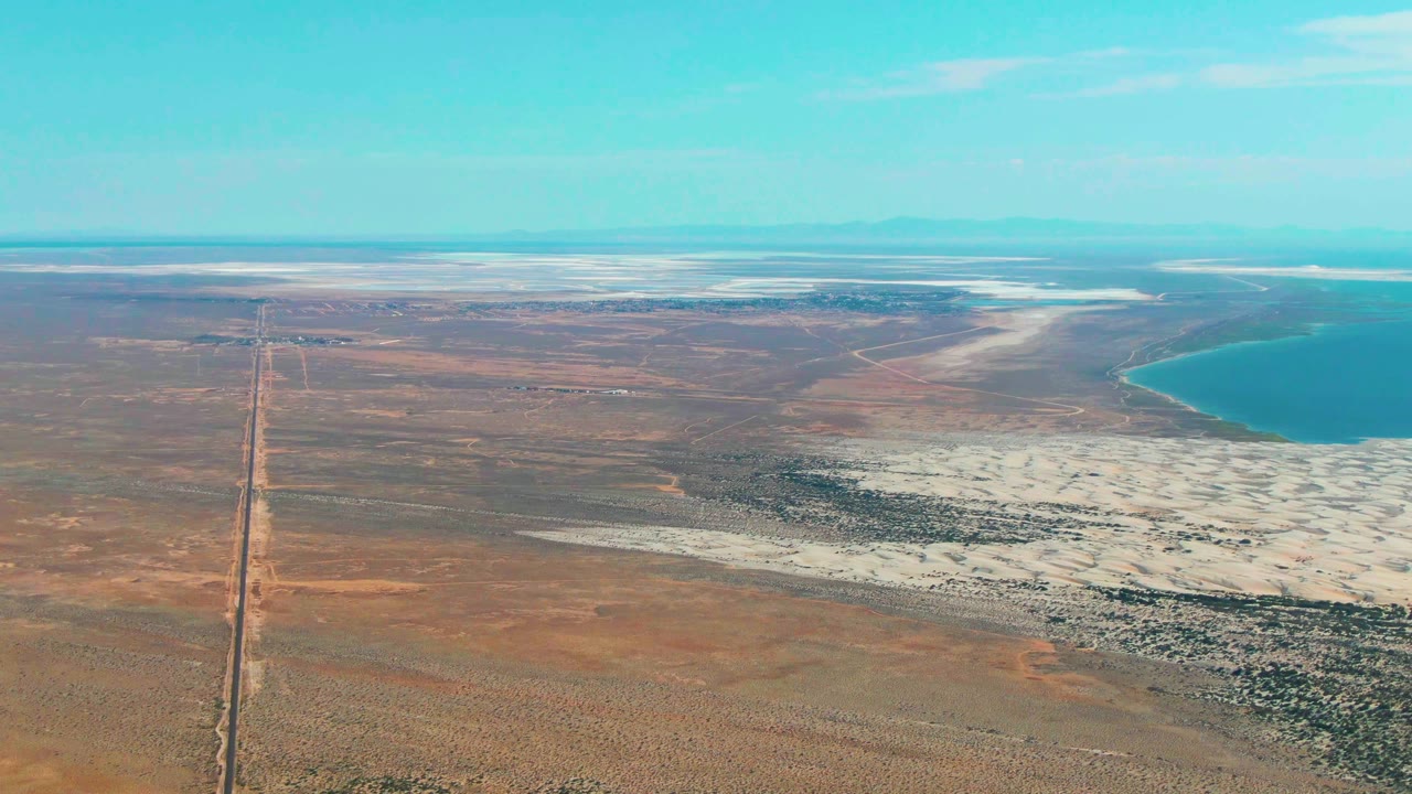 Second frame over Guerrero Negro shows the straight road slightly farther through arid brown terrain, with white salt flats stretching toward blue water on the right and no visible people.