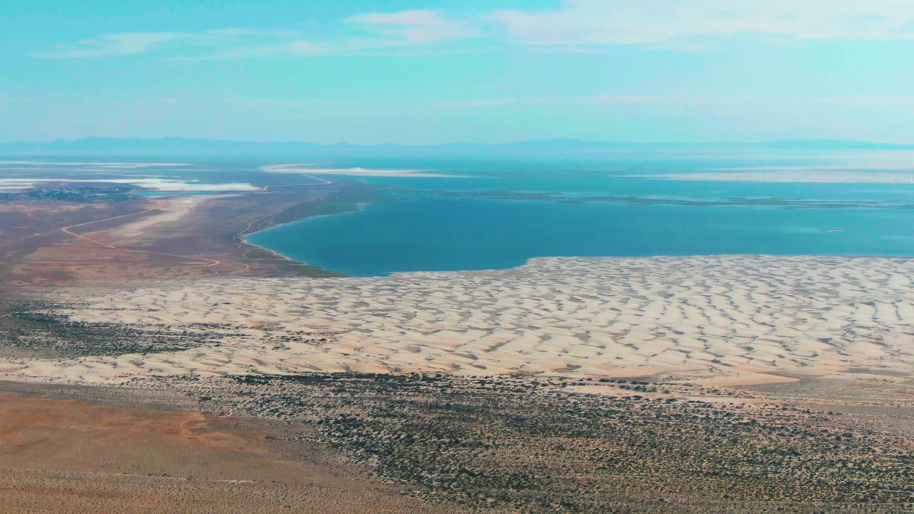 Aerial view of blue water, pale sand, and arid scrubland.