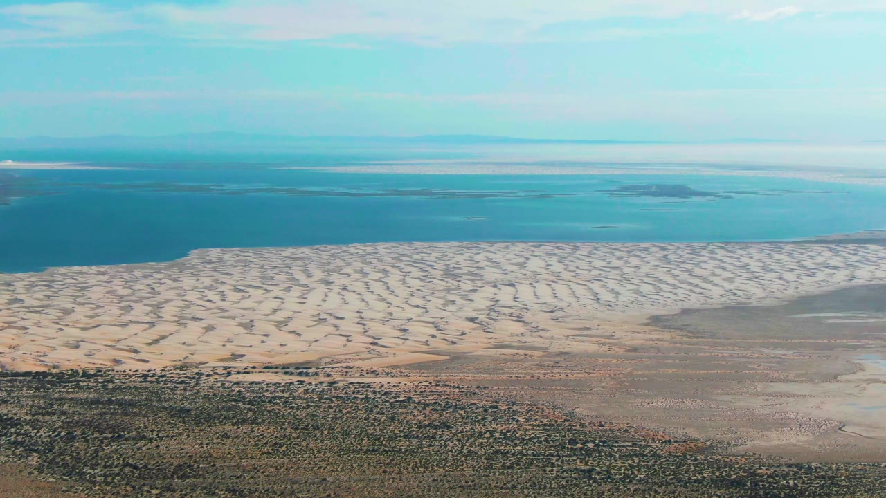 A second aerial view in Guerrero Negro shows the tidal sand band stretching across frame, turquoise water behind it, a low horizon, and no visible people.