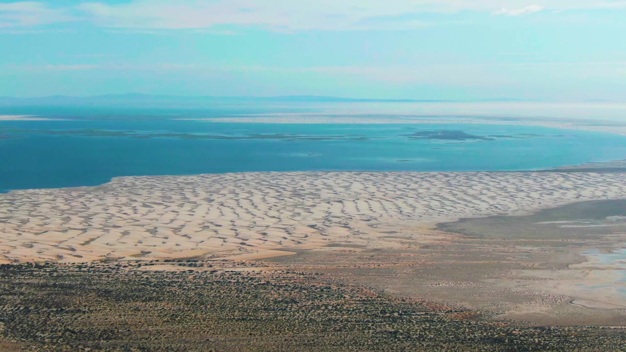 At three seconds, the Guerrero Negro aerial view shows white rippled sand flats, a blue water band to the left and rear, muted foreground terrain, and no visible people.
