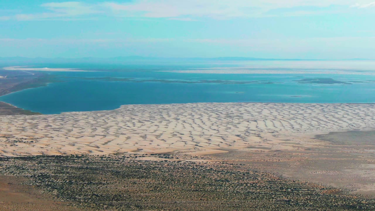 Aerial shoreline with pale sand ridges, blue water, and dry scrub terrain.