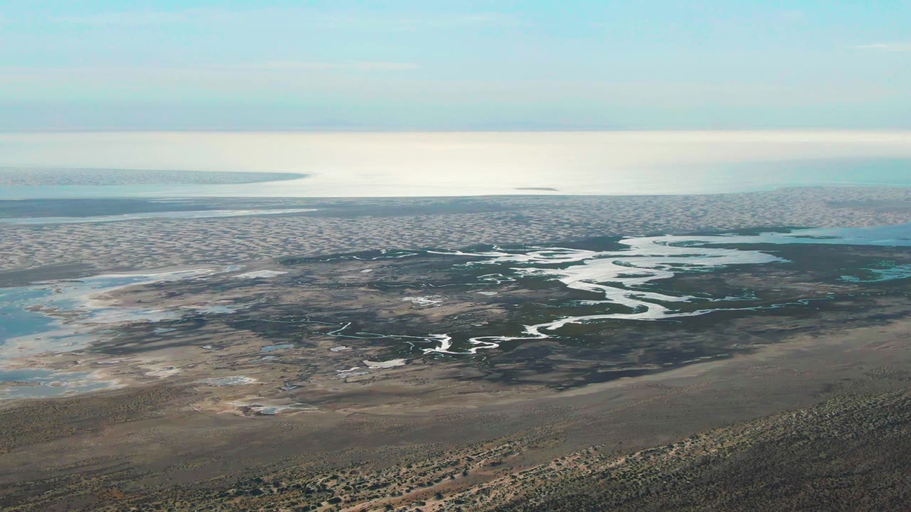 Aerial frame from Guerrero Negro, Baja California Sur, with meandering white-blue water channels crossing dark wetland ground, pale pools at left, and no visible people.