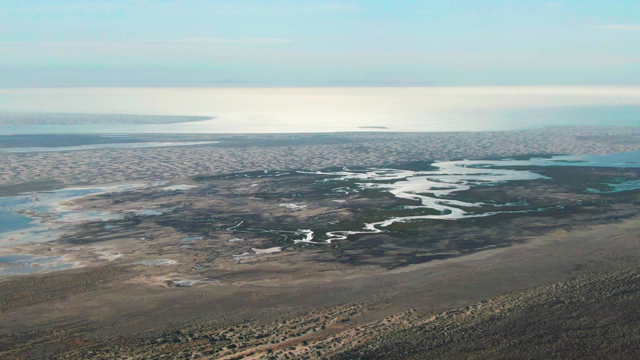 Wide aerial still over Guerrero Negro, Baja California Sur, showing the wetland channels shifted farther across the center of frame, with distant water on the horizon and no visible people.