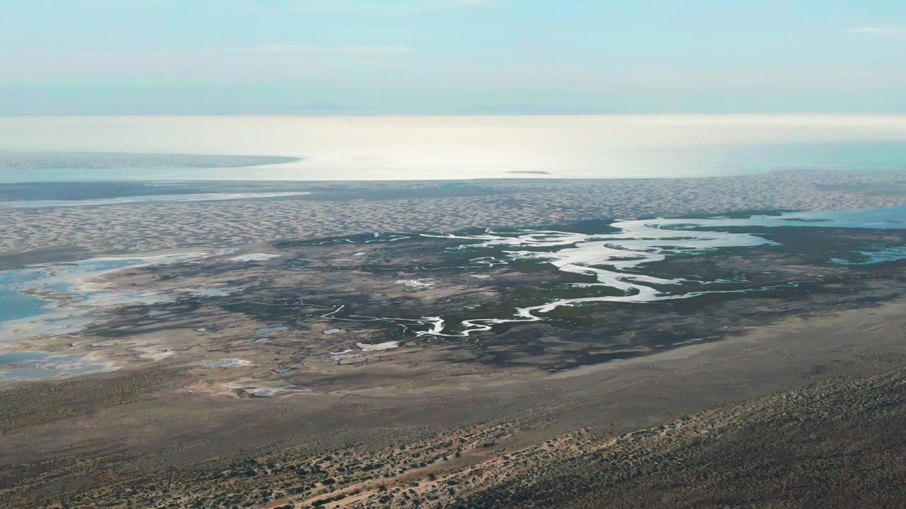 Aerial landscape of bright water channels cutting through dark marsh and brown flats.