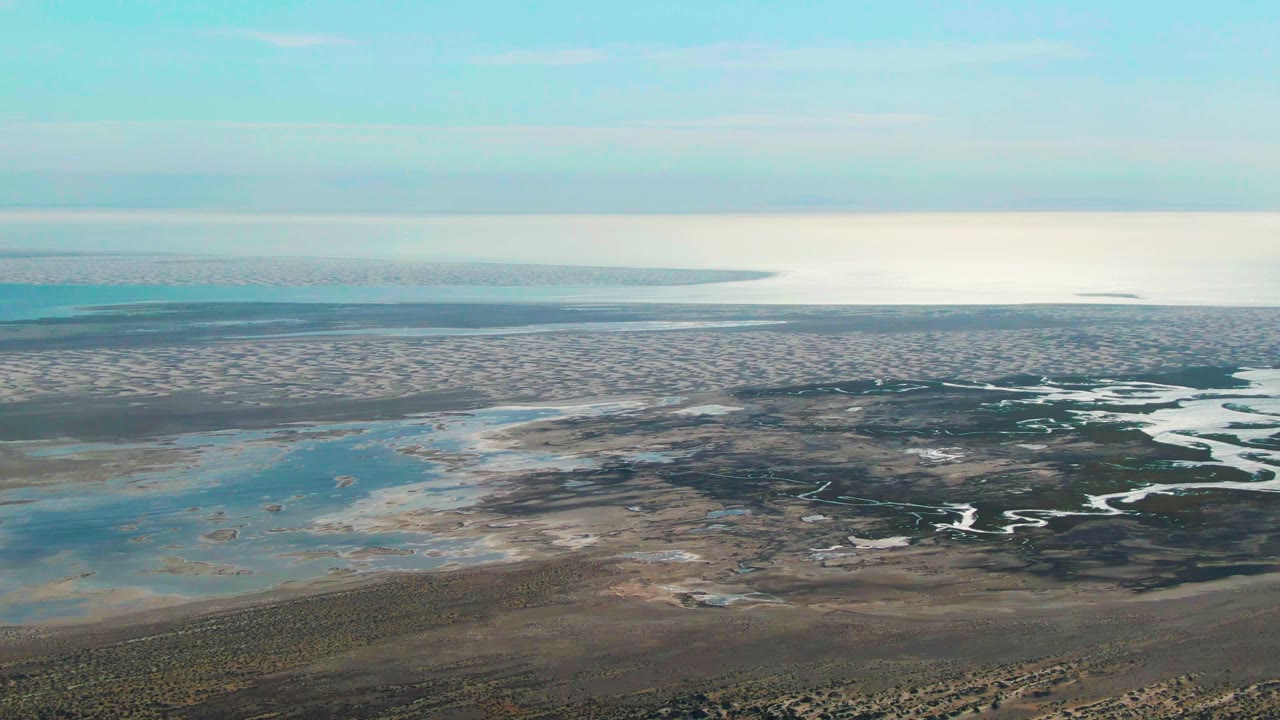 Aerial view of coastal mudflats, shallow water, and distant horizon.