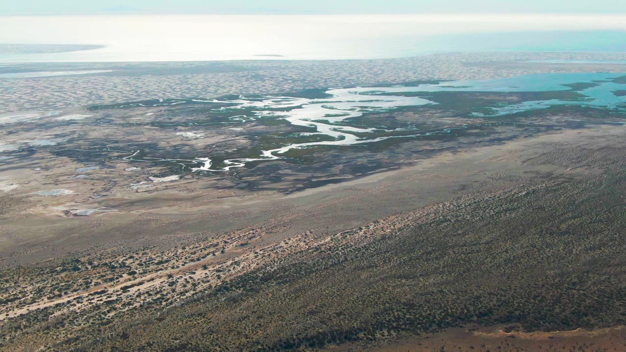 High aerial landscape with scrub-covered ground, pale channels, and blue-green wetland water.
