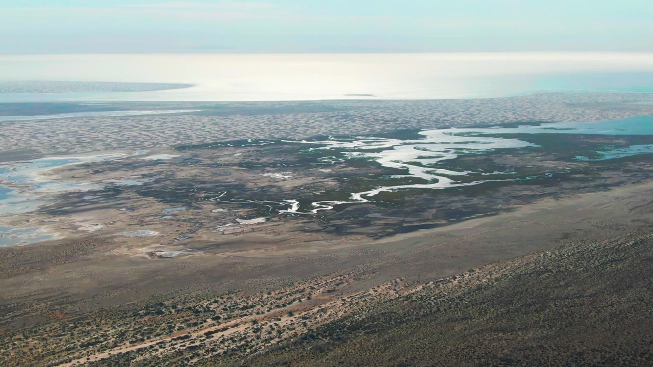 Guerrero Negro aerial frame showing bright river bends crossing dark wetland vegetation, with coastal blue water at the upper right and no visible people.