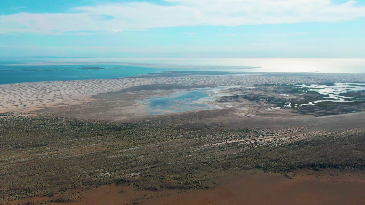 One second into the clip, the Guerrero Negro aerial remains fixed on pale dunes, reflective shallow water, dark tidal flats, low vegetation, and no visible people.